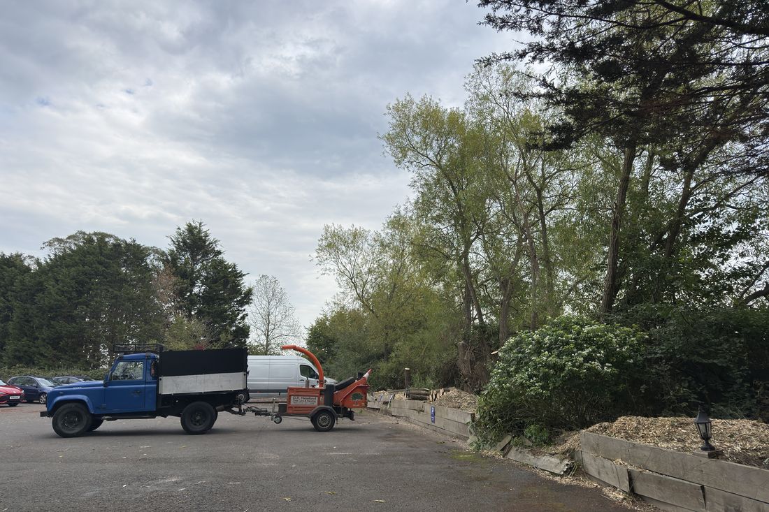 The same car park with the willow removed, wood chip by the wall, and a tipper truck and chipper parked up